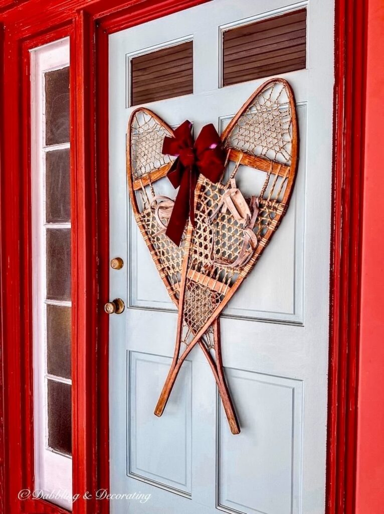 Pair of vintage wooden snowshoes criss crossed on blue front door on red house with burgundy bow.