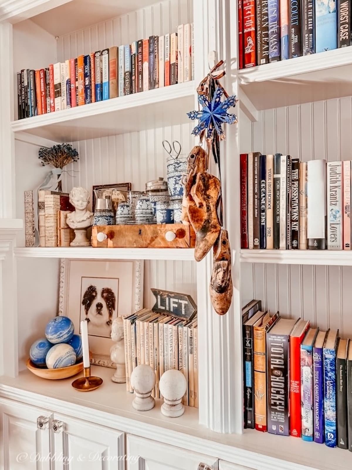 White built-in bookcases with books and vintage decor with hanging vintage cobbler shoe molds for the holidays.