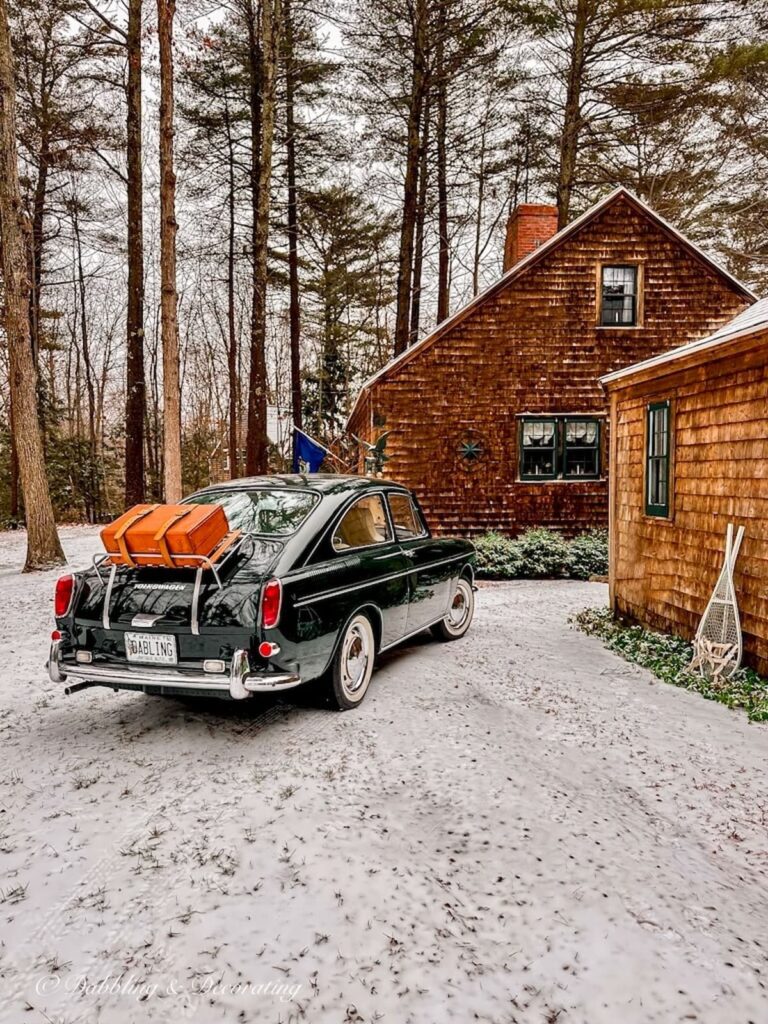 Antique VW Fastback car in front of rustic house in snowy scene.