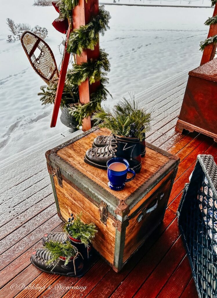 Vintage black ski boots with evergreens on vintage trunk in an Après ski theme porch.