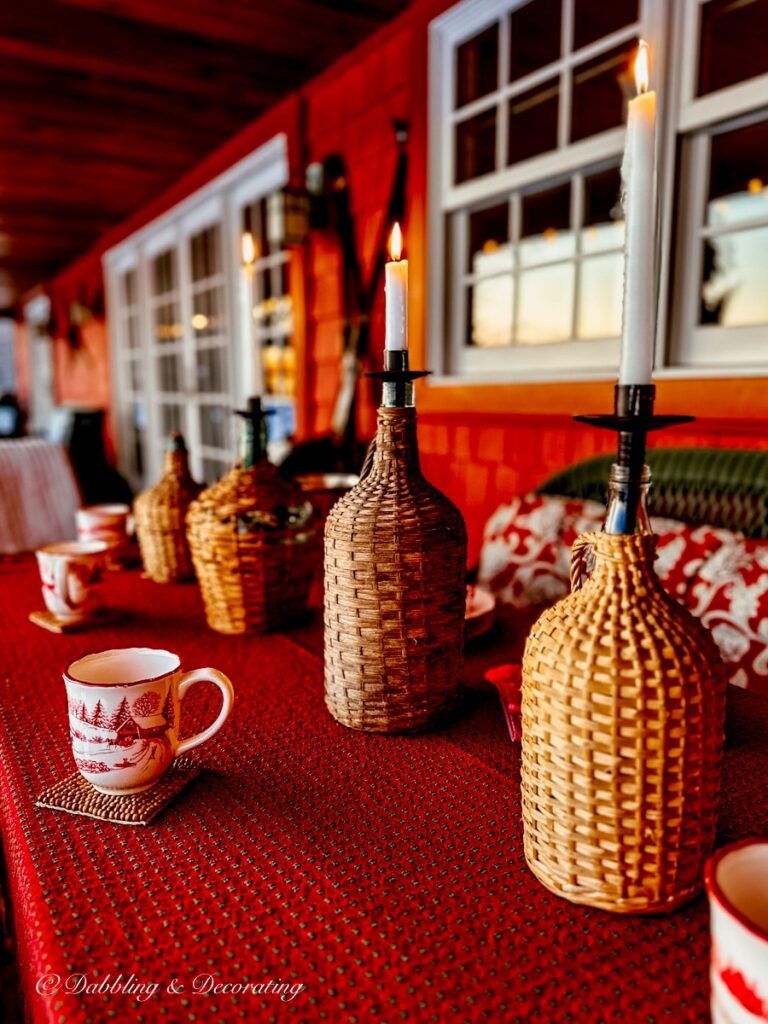 Three vintage demijohn bottles on red wooden table with candles on Après ski theme porch.