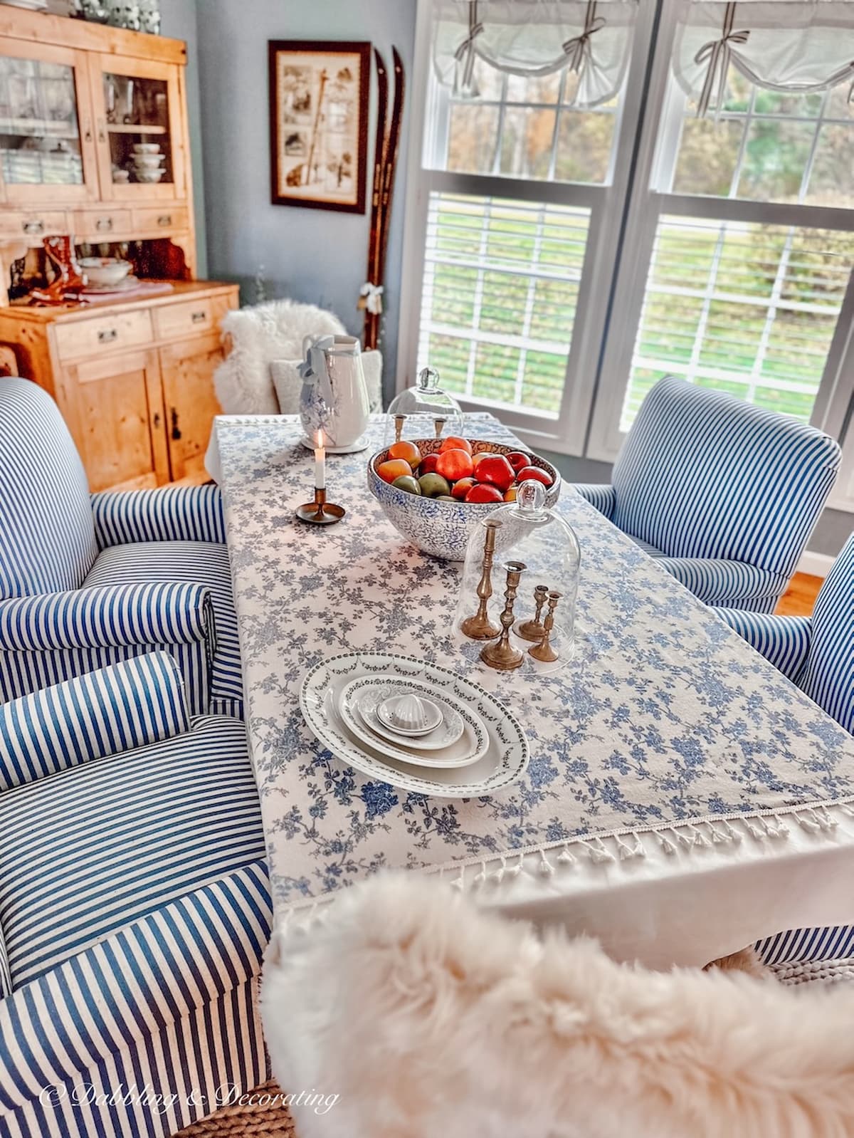 Dining room with blue and white chairs and tablecloth with three large window wall.