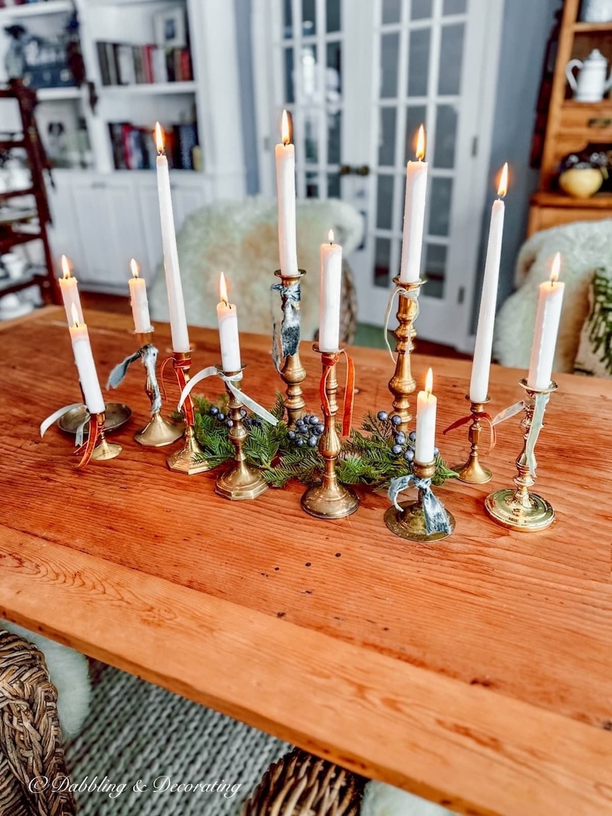 A collection of vintage brass candlesticks on pine wood dining room table lit with ribbons.