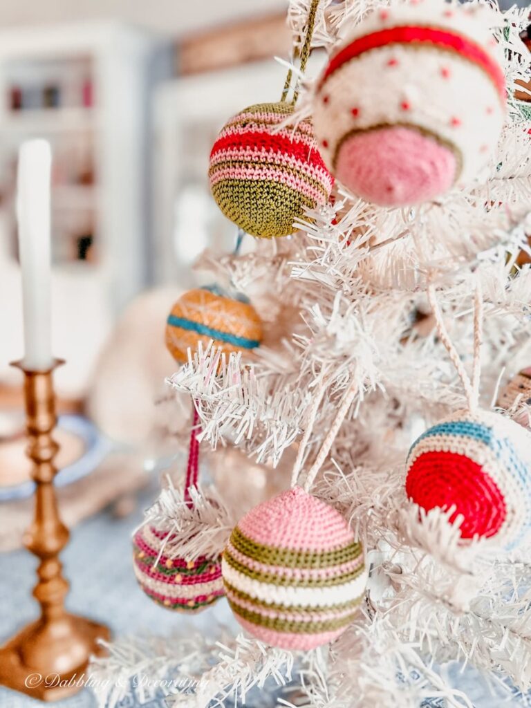 White vintage Christmas tree with colorful needlepoint vintage ornaments and brass candlestick and white candle as center of table.