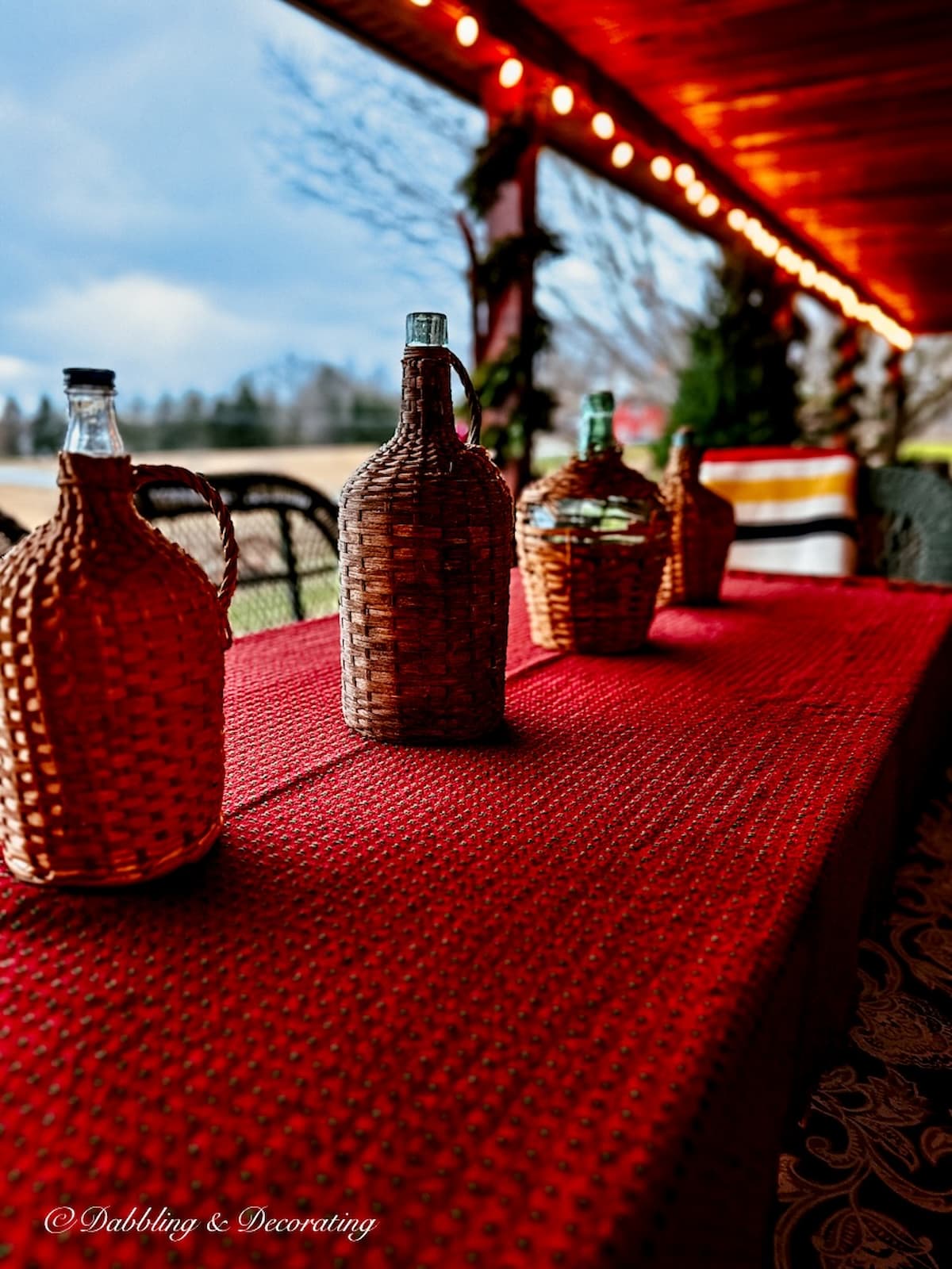 Four vintage Demijohn bottles on red Mountain Weaver tablecloth for the holidays on outdoor porch.