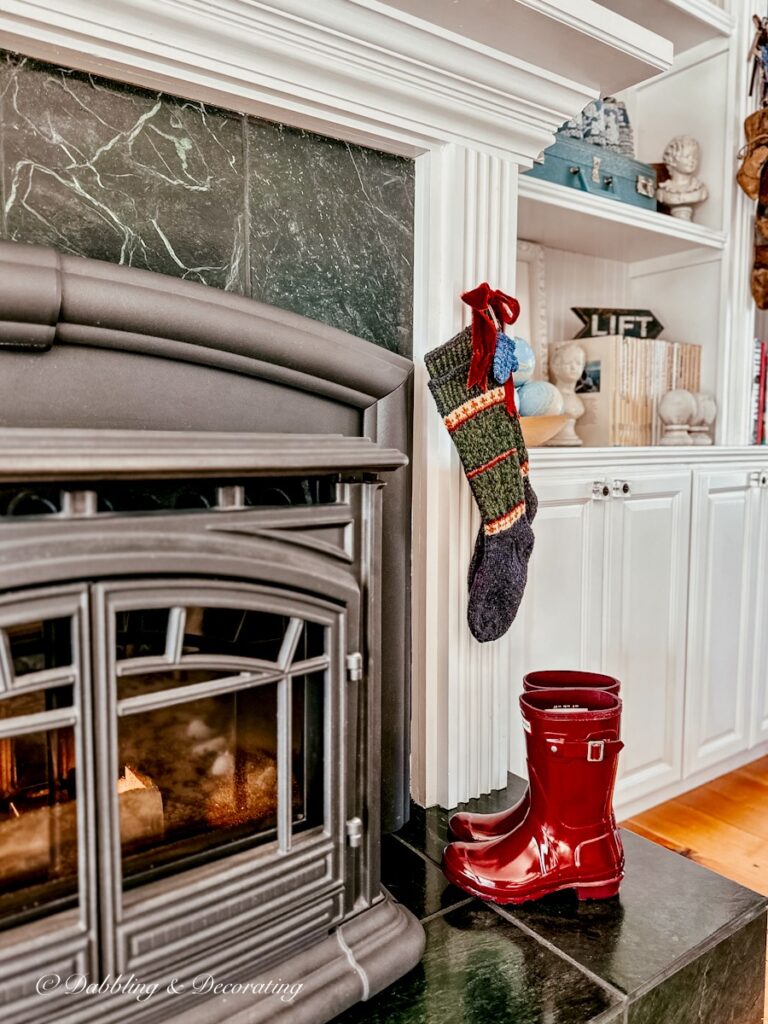 Hand Knit stockings hanging at fireplace with burgundy bow and red boots.