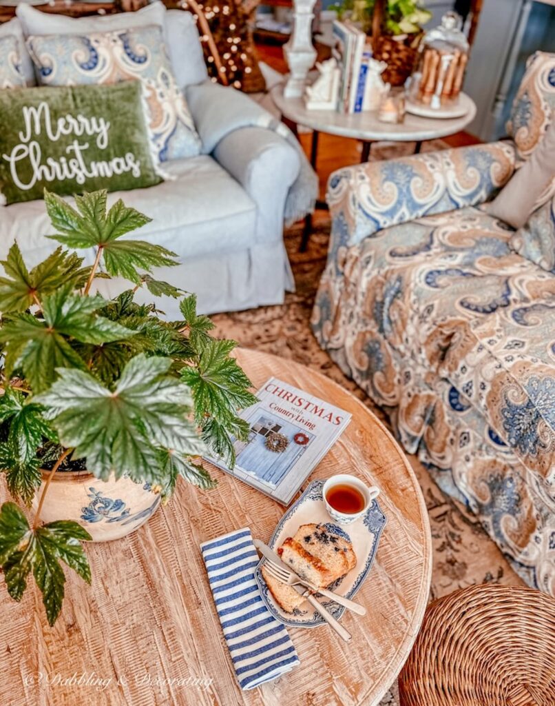 Blue and white cozy styled living room with Johnson Brother's tea and toast vintage dish with blueberry cake and tea, Christmas with Country Living Book ad green plant in crock on round coffee table.