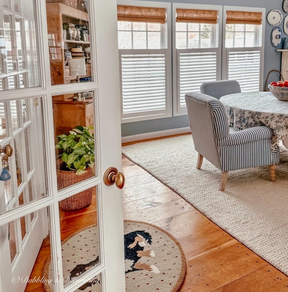 Dining room with open white French door overlooking three windows with bamboo shades.