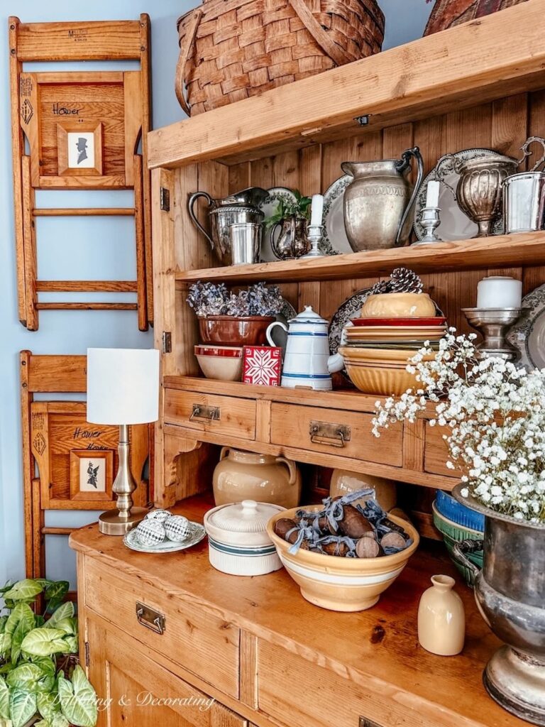 Vintage hutch with vintage silver and pottery next to vintage chairs hanging on wall with small silhouettes perfect Eclectic Interiors.