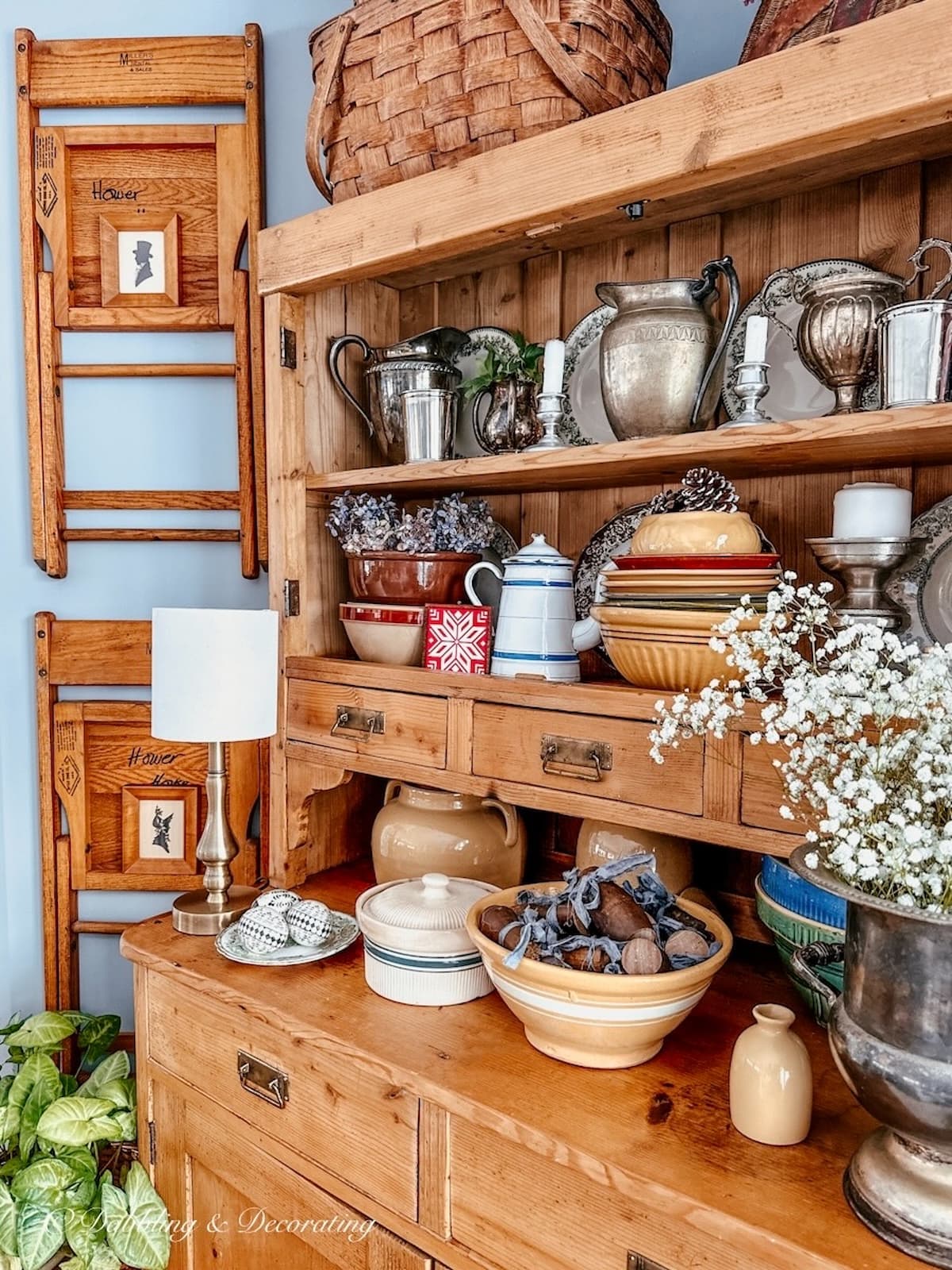 Vintage hutch with vintage silver and pottery next to vintage chairs hanging on wall with small silhouettes.