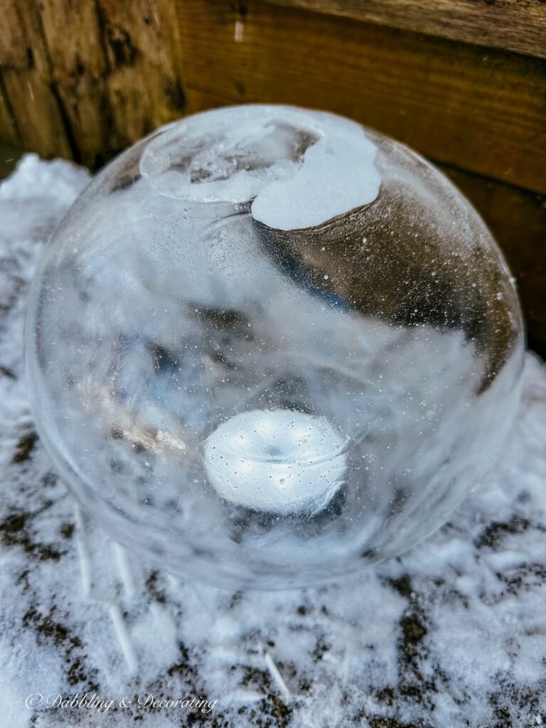 Round ice lantern globe on top of LED light on snow filled step.