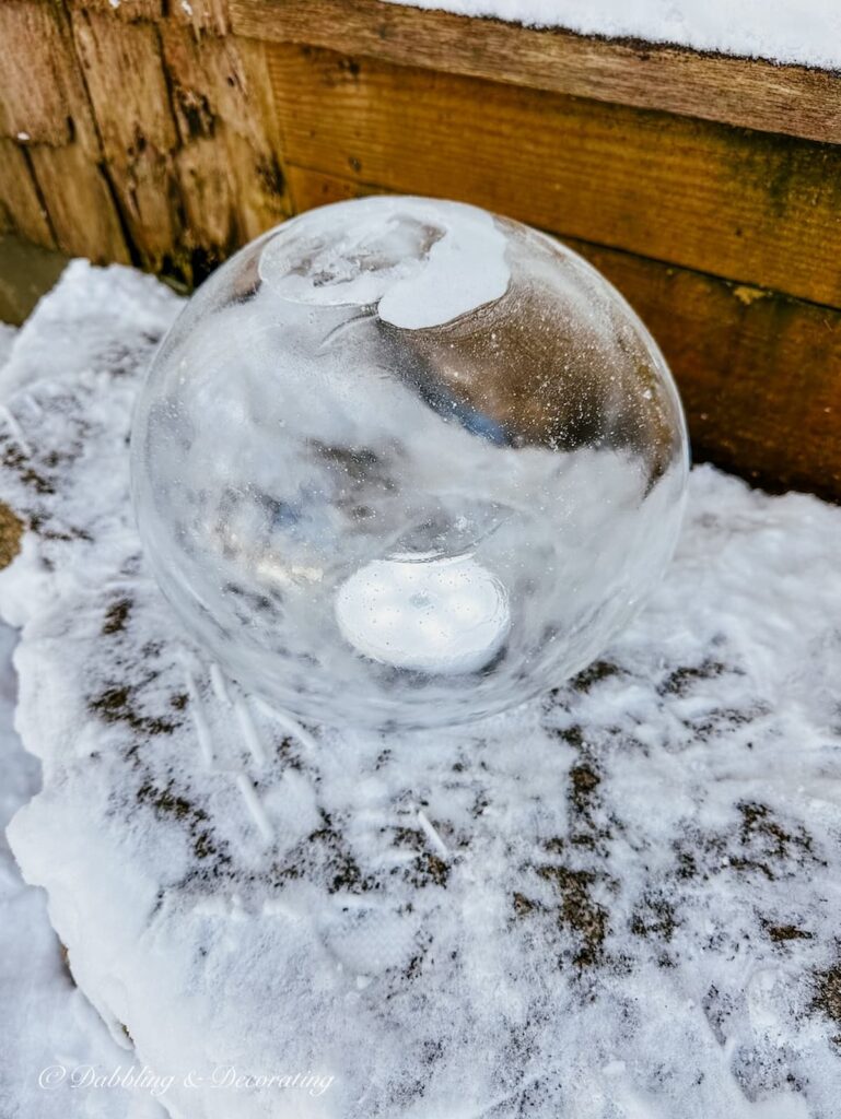 Ice lantern with LED light inside on snowy front step outside.