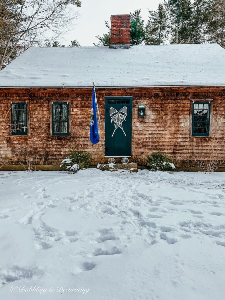 Cedar Shakes home with green door and snowshoes with Maine flag in the snow.