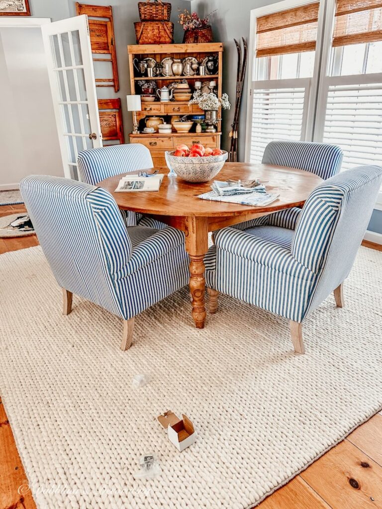 Dining room with blue and white striped chairs around pine table with hutch on white rug and small scattered boxes on floor.