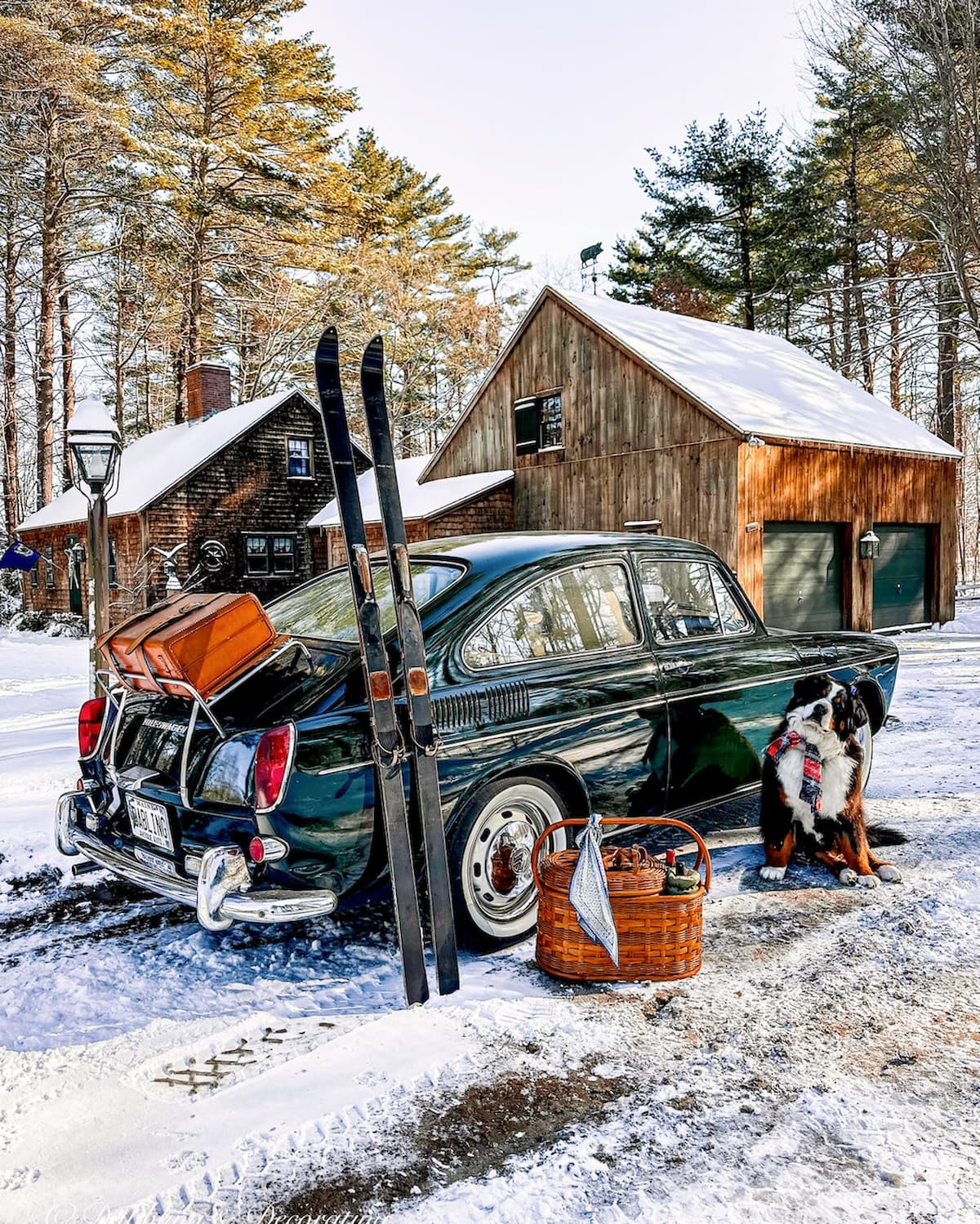 1968 VW Fastback in green with vintage HEAD skis, picnic basket and luggage on trunk with Bernese Mountain Dog in front of cedar shakes home on a snow day.