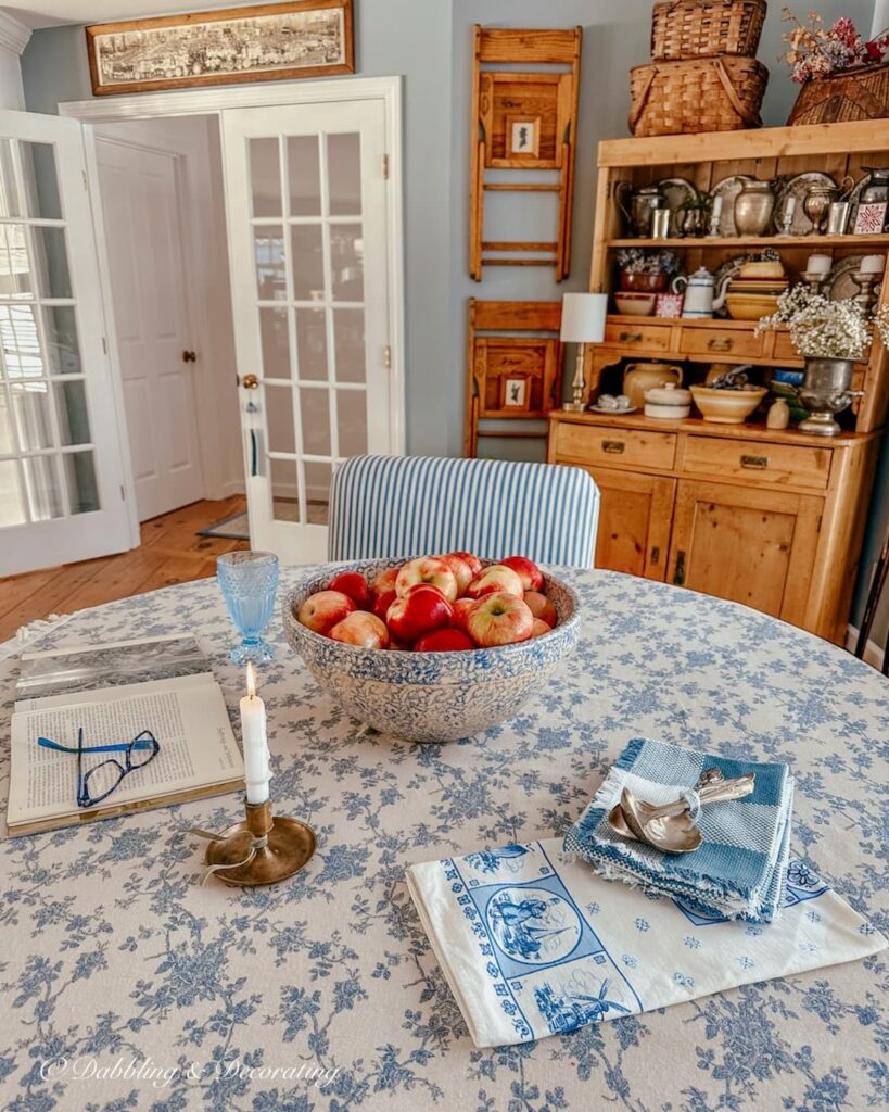 BLUE AND WHITE DINING ROOM STYLED TABLE WITH BOWL OF APPLES, VINTGE WALL DECOR AND VINTAGE HUTCH .