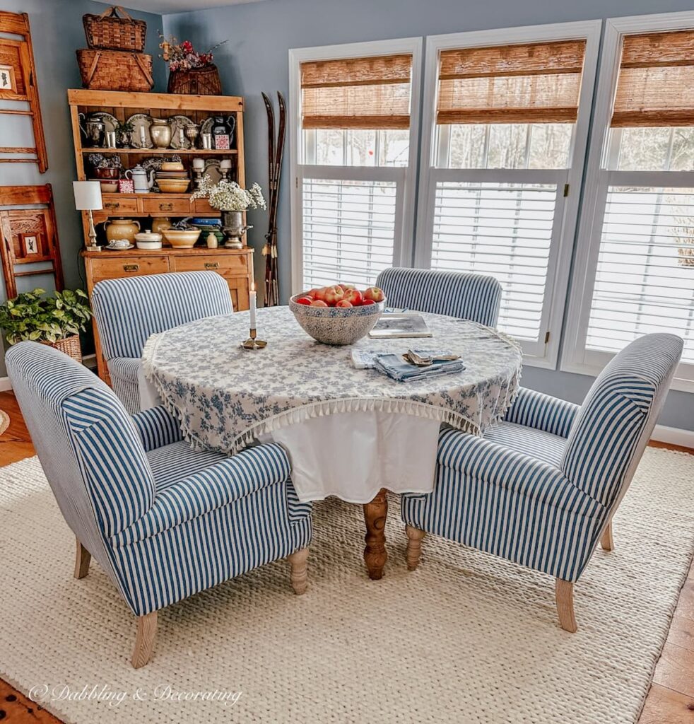 Blue and white dining room with bamboo shades on three windows next to vintage styled hutch.