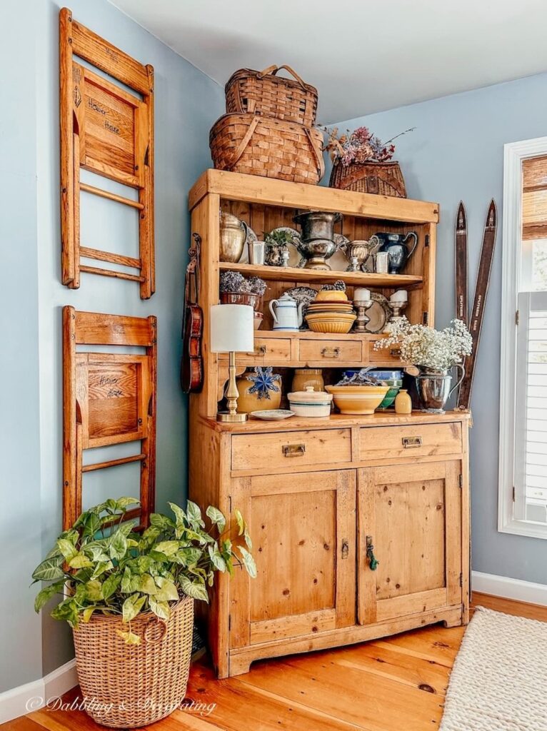 Vintage Pine hutch in dining room corner with vintage wall decor chairs hanging and basket with plant.