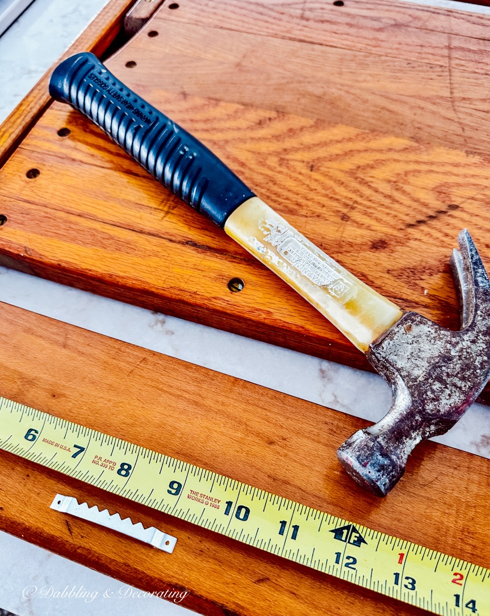 Hammer, tape measure, and sawtooth hanger on front of old chair to hang in vintage wall decor.