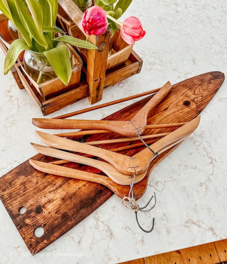 Vintage wooden coat hangers resting on antique trapper's fur stretcher board on kitchen counter top with pink tulips.