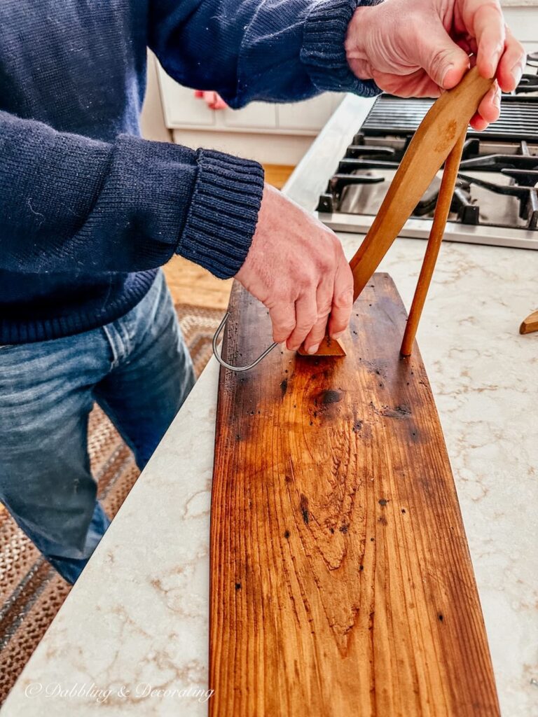 Person holding a half cut vintage wooden clothes hanger onto a wood board.