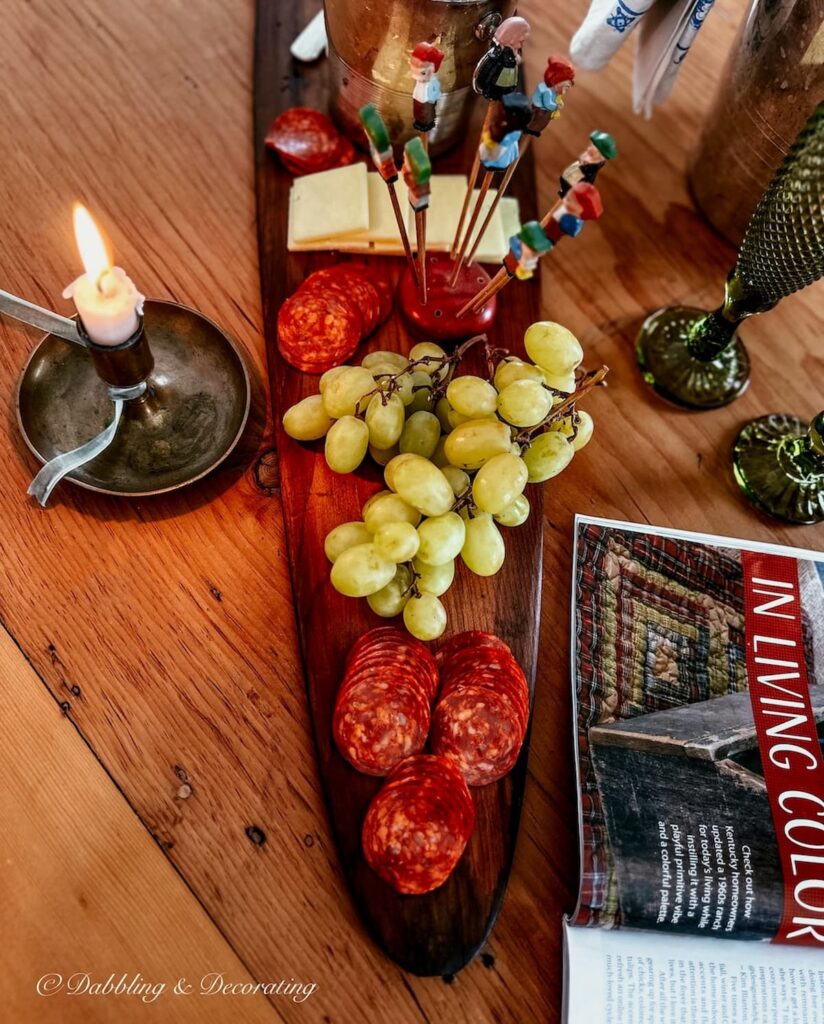 Charcuterie board on antique trapper's board with lit candle and snacks.