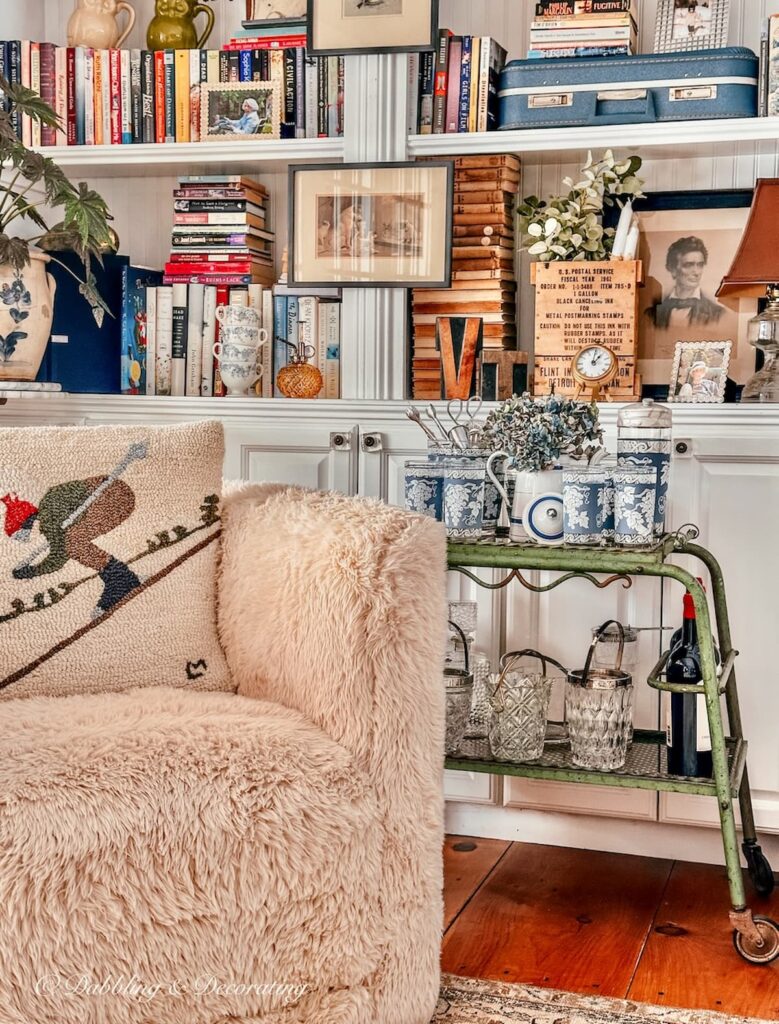 Antique bar cart in Eclectic Interiors living room next to sheepskin chair and eclectic style bookshelves.