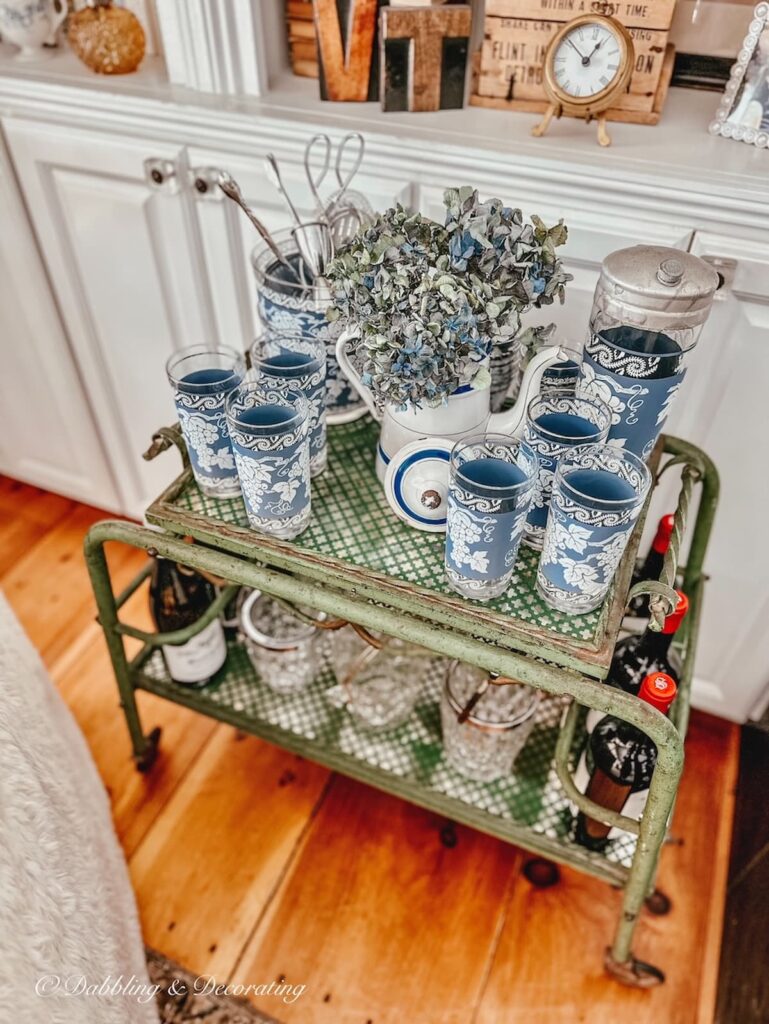 Blue and white Parisian teapot with vintage Jeanette barware on antique bar cart with blue hydrangeas as side table in living room.