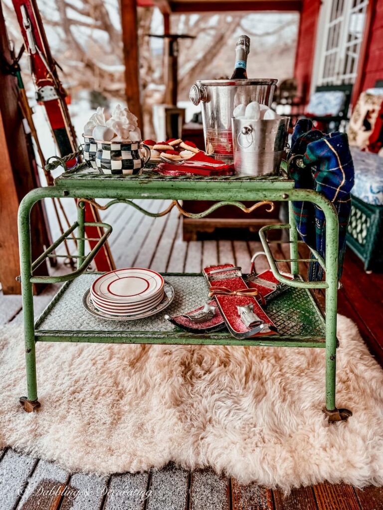 antique green bar cart on sheepskin rug on winter styled porch for apres' ski.