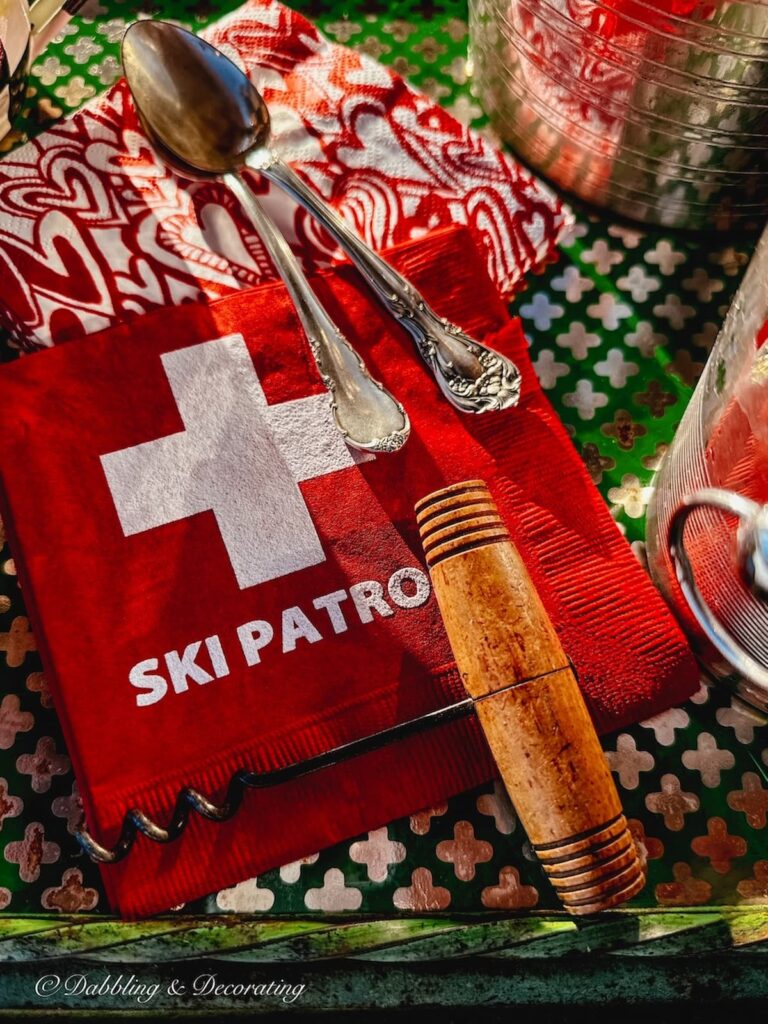 Ski Patrol Swiss Cross napkins, vintage wine cork and silver spoons on antique bar cart outdoors.