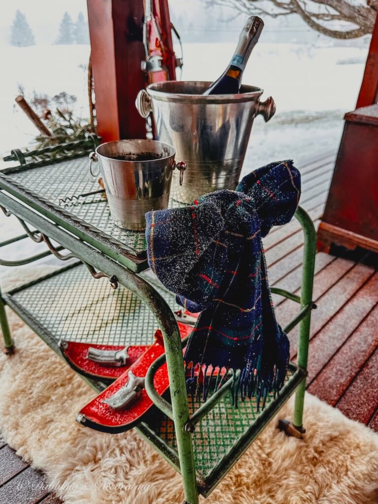 Antique bar cart with plaid blue scarf, silver ice buckets on outdoor covered winter porch.