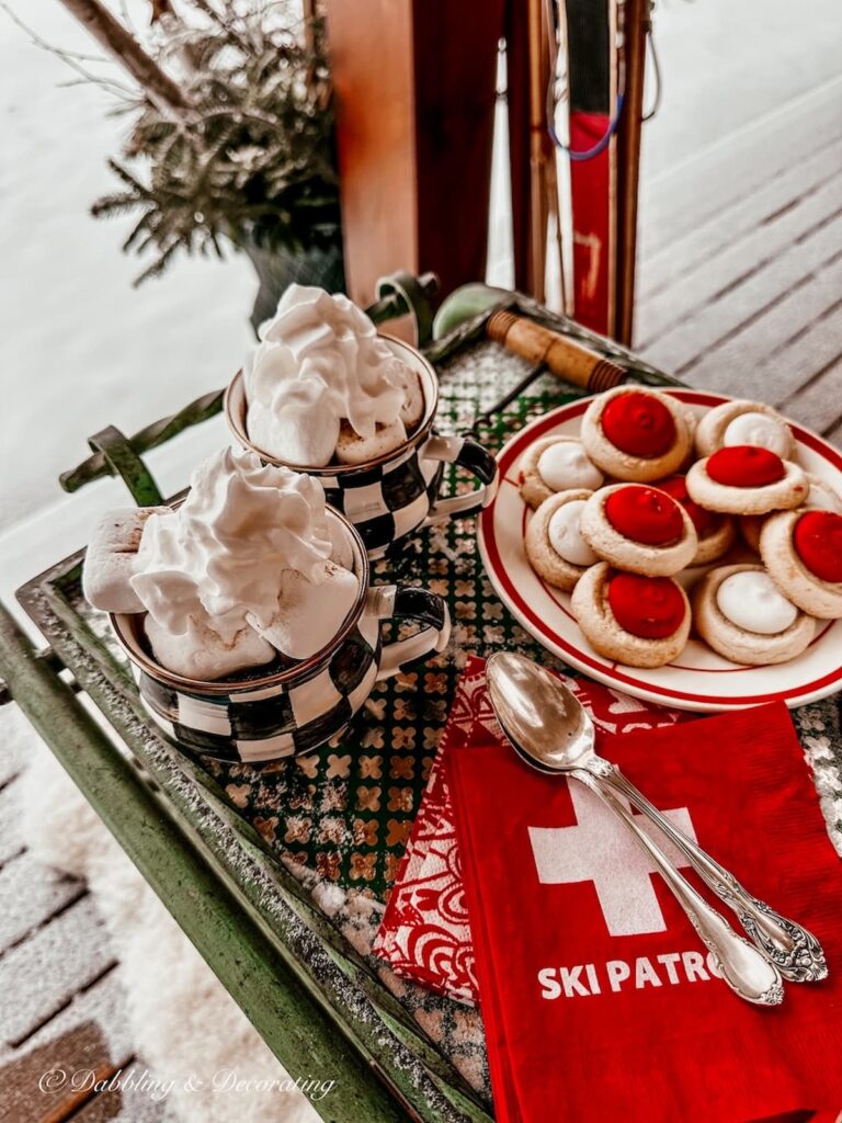 two mugs of hot chocolate and whipped cream on nordic style bar cart on snowy porch scene.