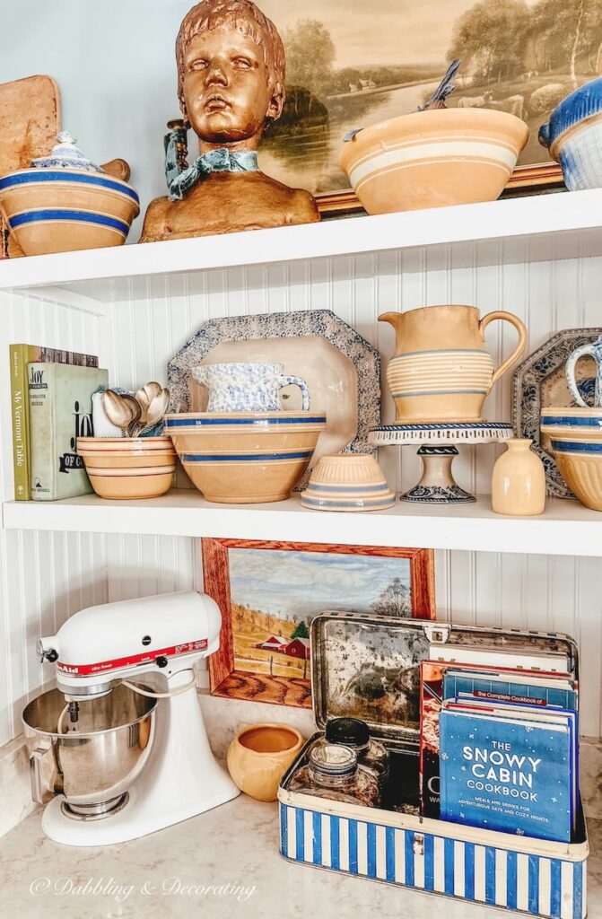 Open white kitchen shelving with antique yellow ware displayed.