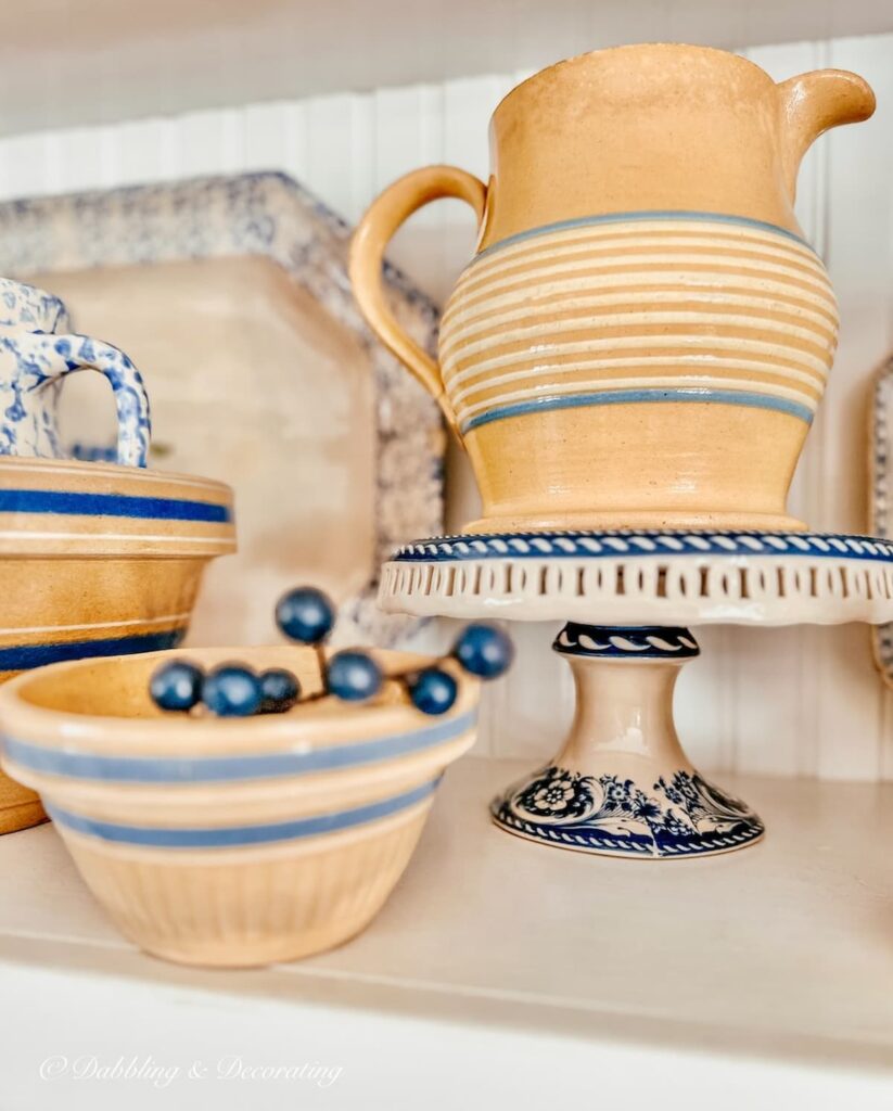 Antique yellowware with blue stripes on vintage cake stand on kitchen shelving with other yellow ware.