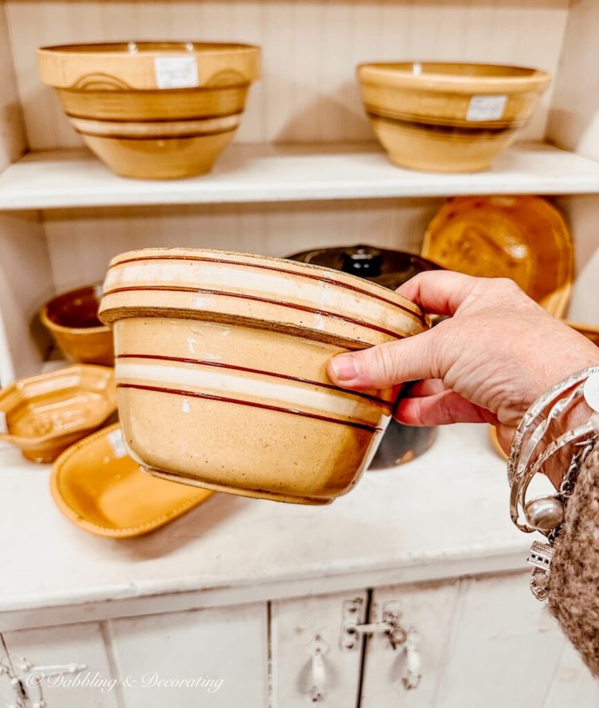 Antique yelloware bowl with brown and white stripes in hand at antique store in front of yellow ware decorated hutch.