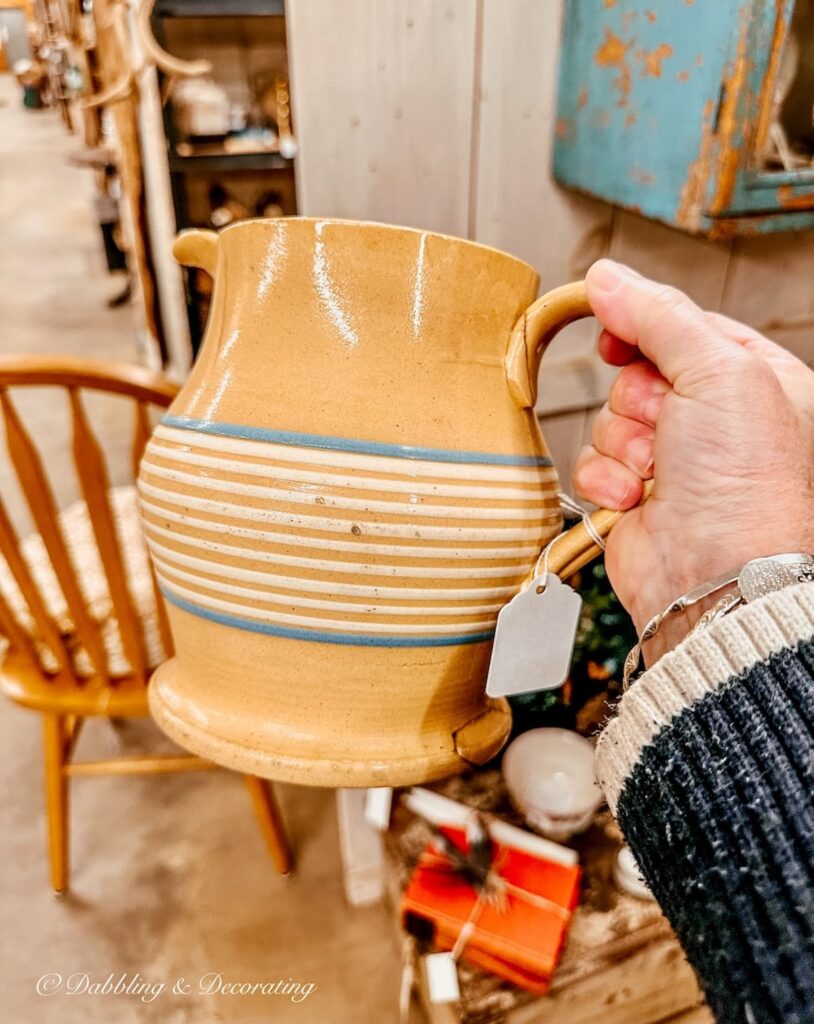 Antique yellow ware pitcher with blue and white strips in hand at antique store.