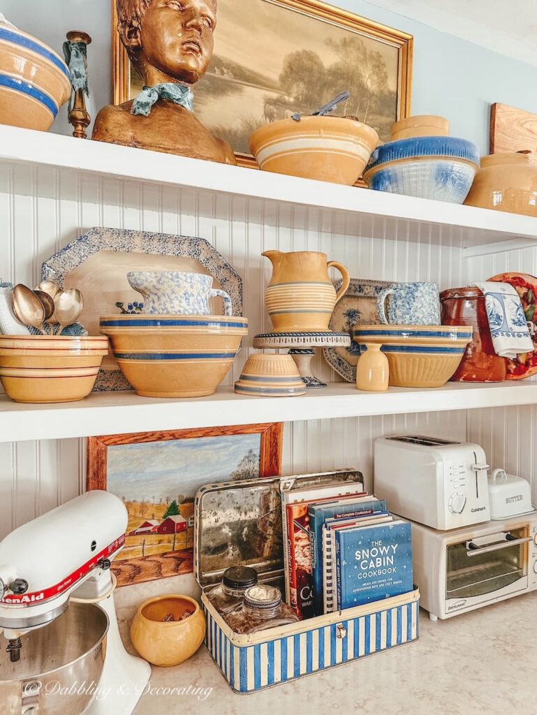 Open white kitchen shelving decorated with antique yellow ware.