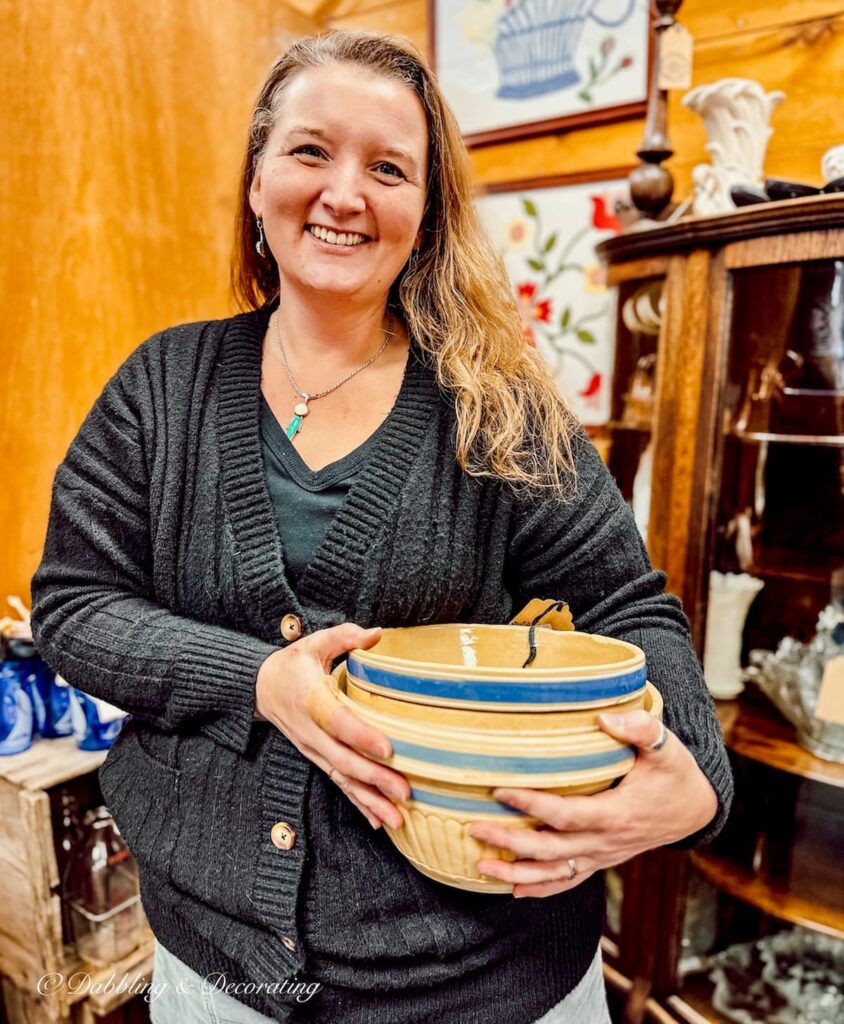 Woman in antique store holding a stack of yellow ware with blue stripes in antique store.