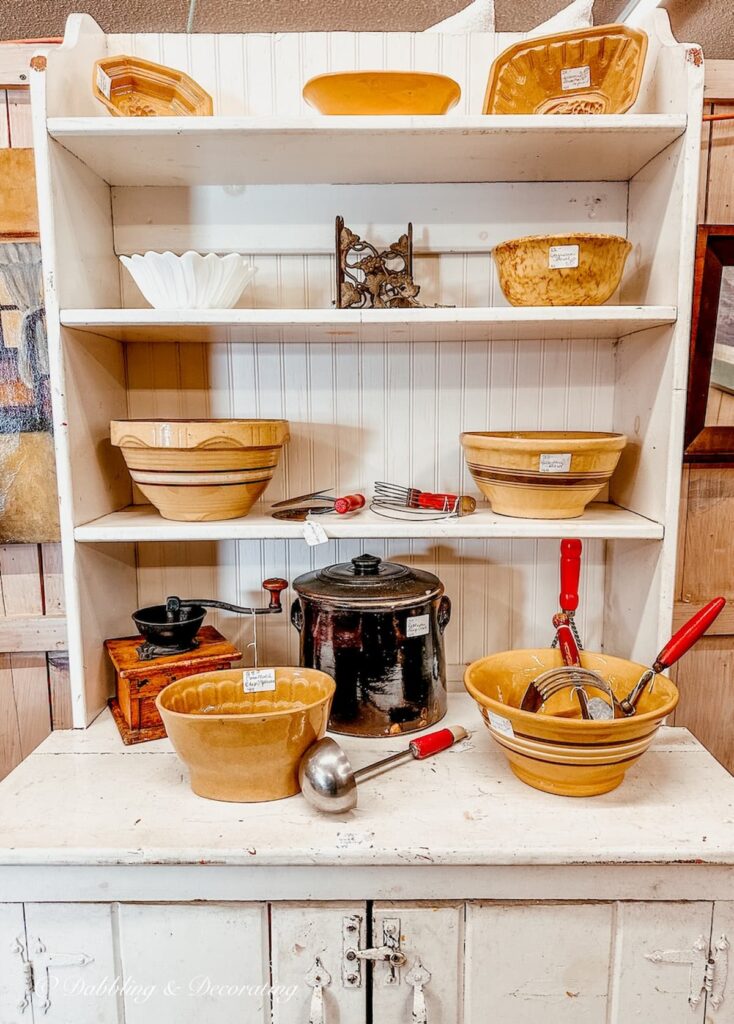 White vintage cupboard with bowls of different yellow ware and other antique collectibles.