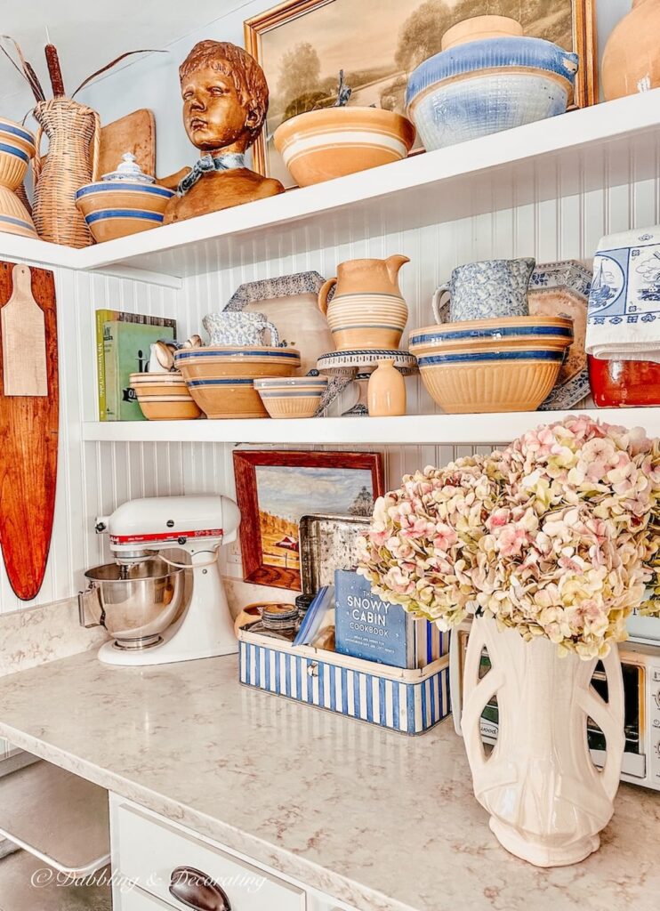 Antique yellow ware with blue accents on open white kitchen shelving.