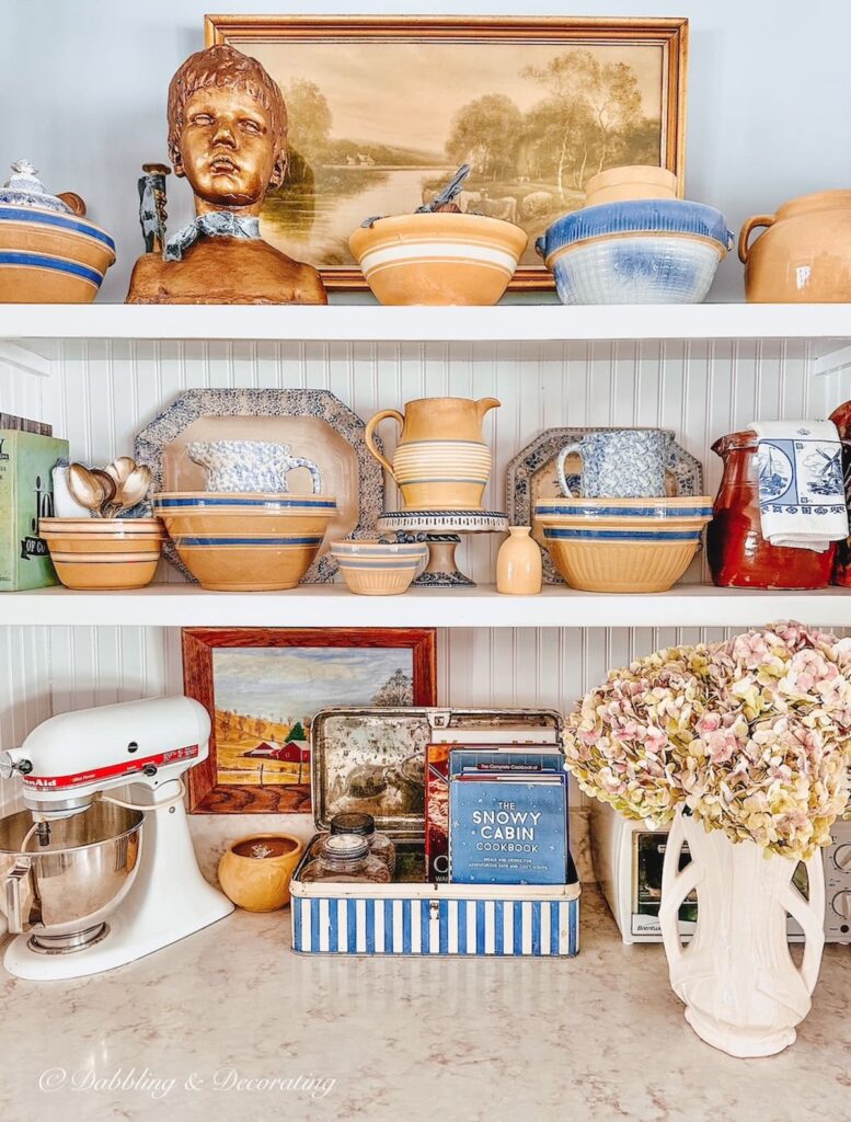 Antique yellow ware with blue accents on open white kitchen shelving.