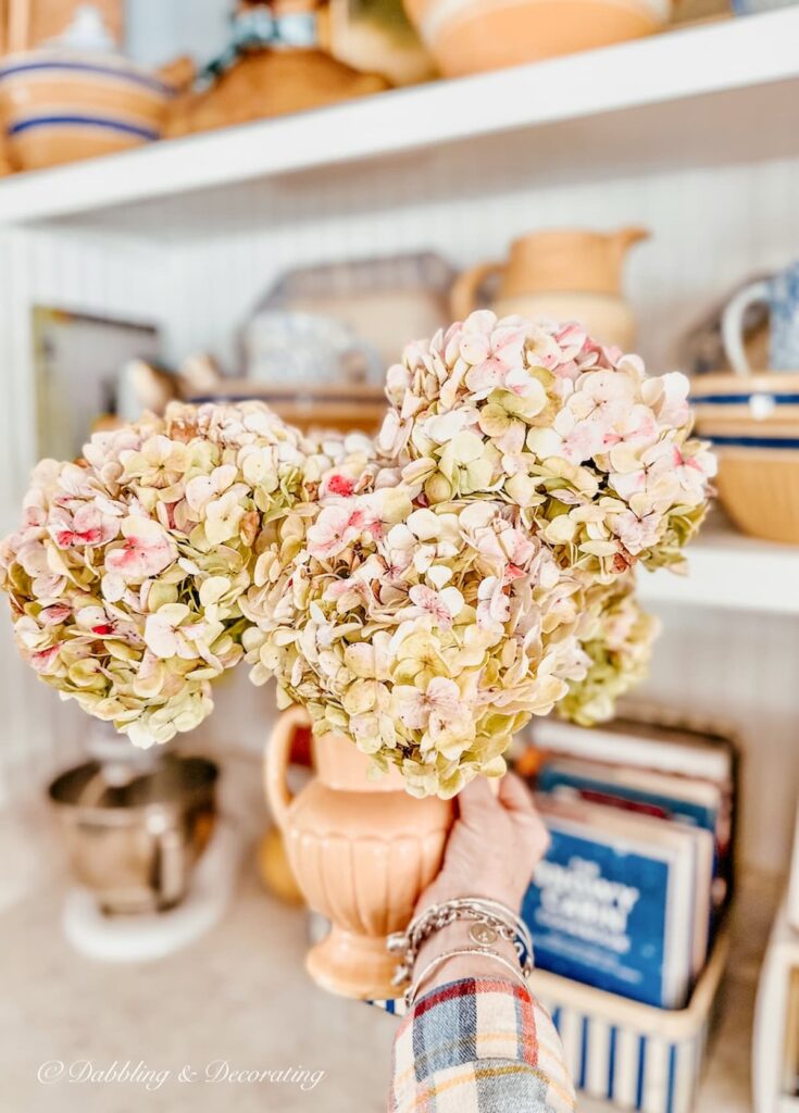 Vintage Yellow McCoy vase with pink hydrangeas in hand in kitchen.