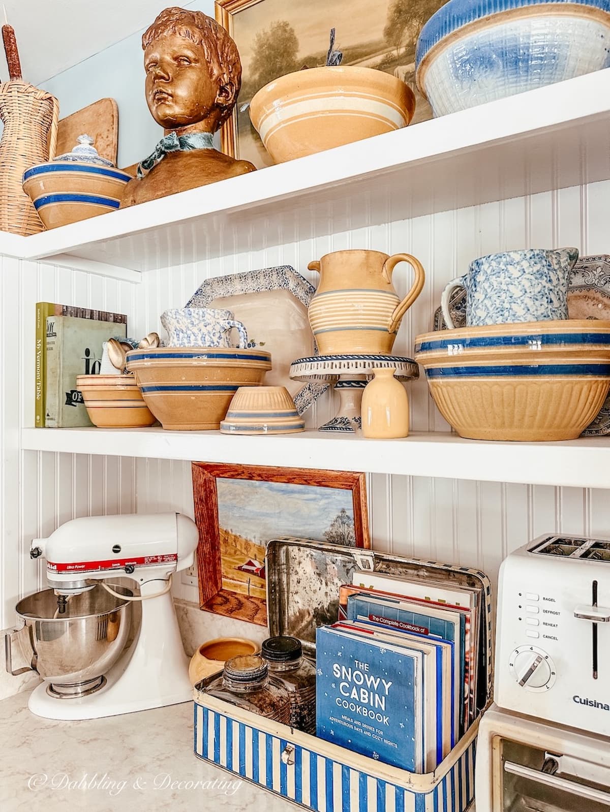 White open kitchen shelving decorated with vintage yellow ware, cookbooks, and more.