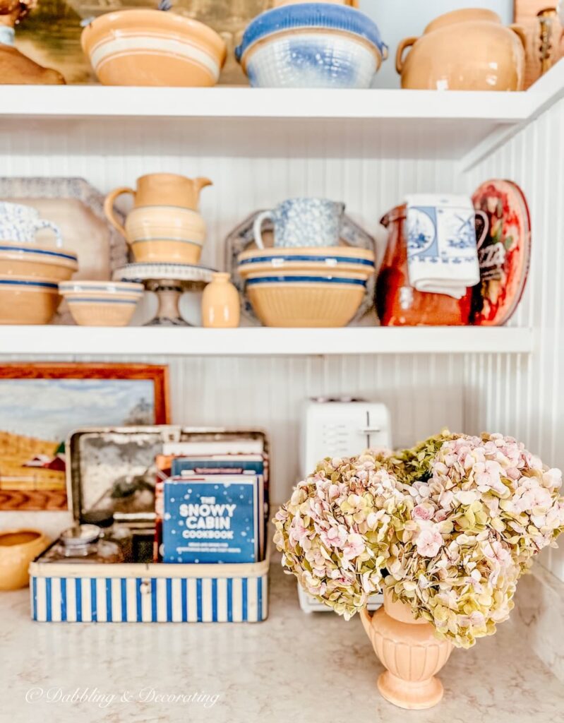 Vintage yellow ware pottery on white open kitchen shelving and vase of pink hydrangeas.