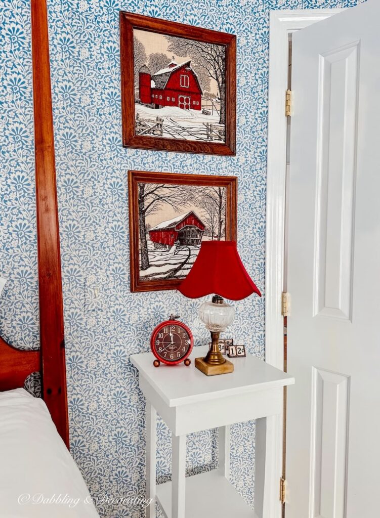 Two Kay Dee Linen Red winter scenery prints in wooden frames on wall in bedroom with red lamp and blue wallpaper.