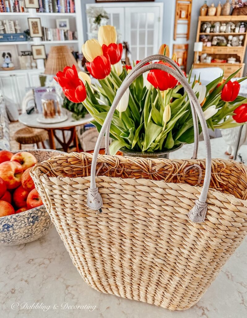 Basket with handles on kitchen counter with tulip bouquet and bowl of apples in eclectic interiors.