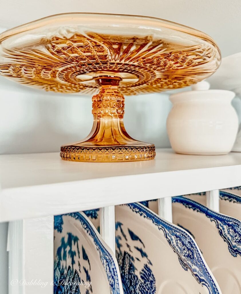 Amber glass cake stand on top of white dish rack in eclectic interiors.