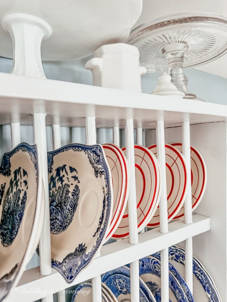 Amber glass cake stand with blue and white vintage tea and toast plates and red and white small plates in white dish rack in eclectic interiors kitchen.