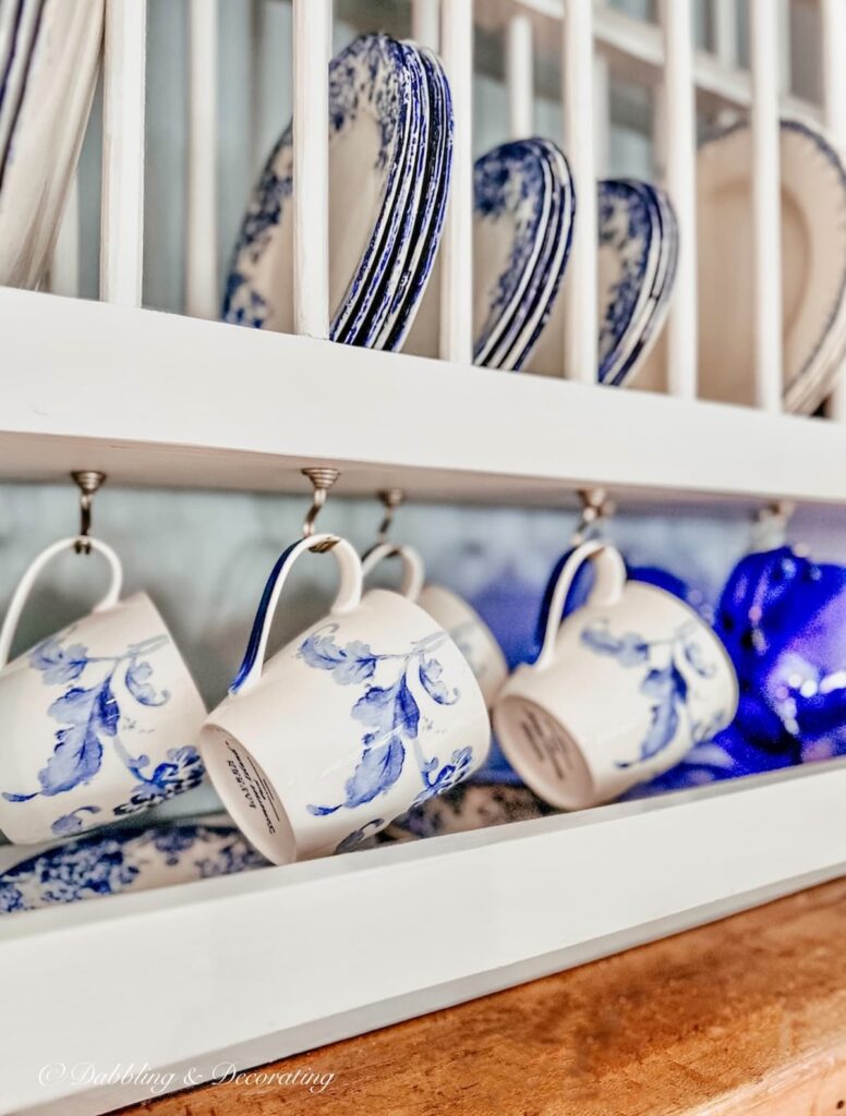 Blue and white mugs and dishes displayed in white eclectic interiors dish rack in kitchen close up.