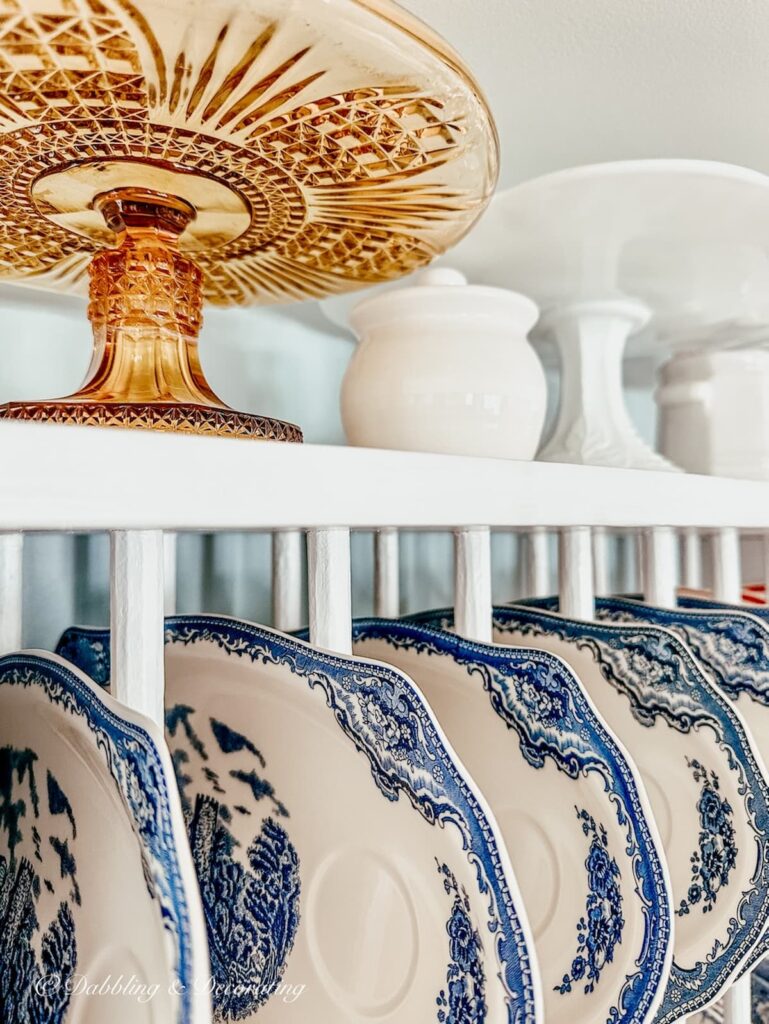 Amber glass cake stand with blue and white vintage tea and toast plates in white dish rack in eclectic interiors kitchen.